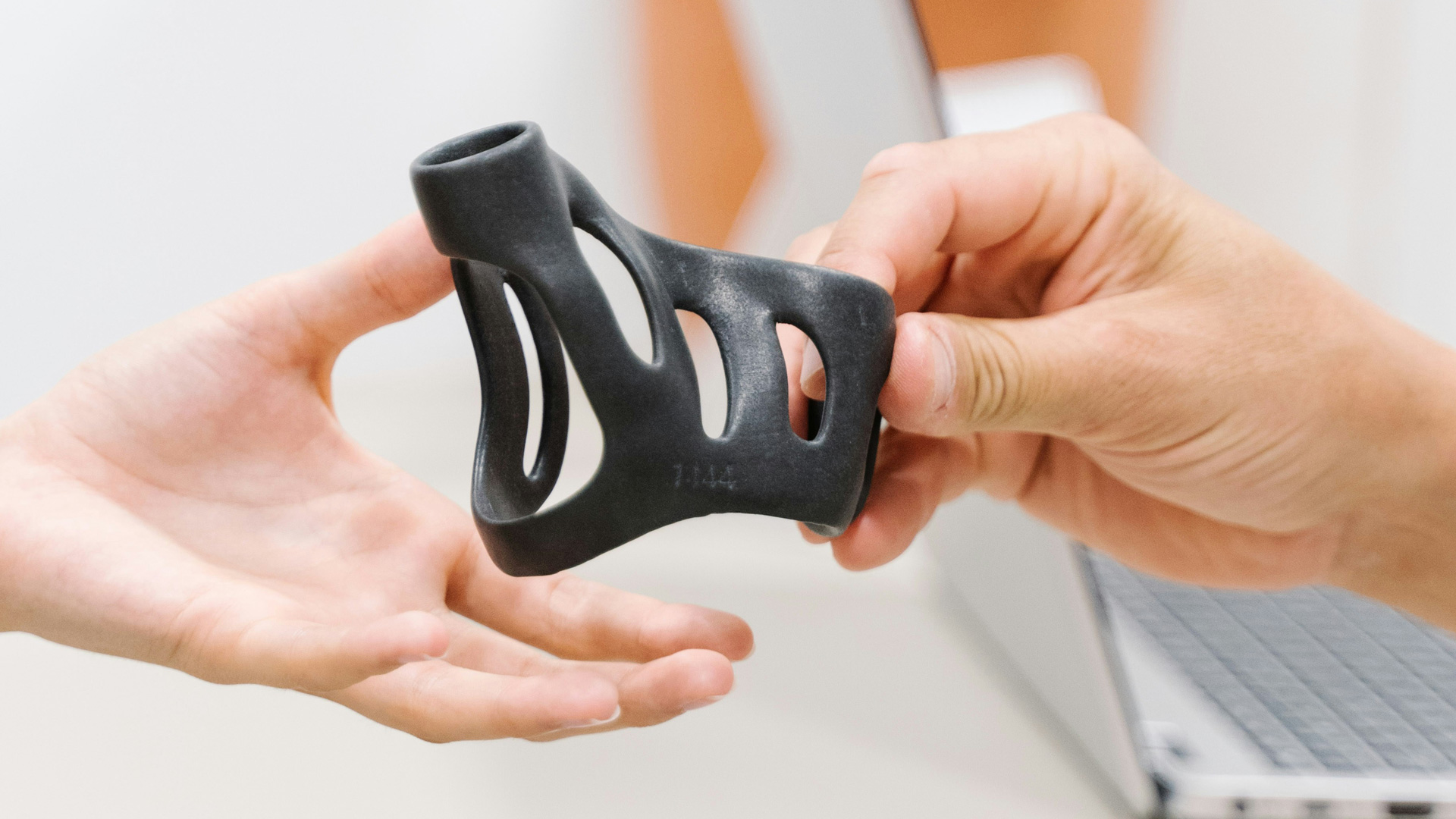 Close-up of two hands passing a black silicone accessory with curved cut-out slots.