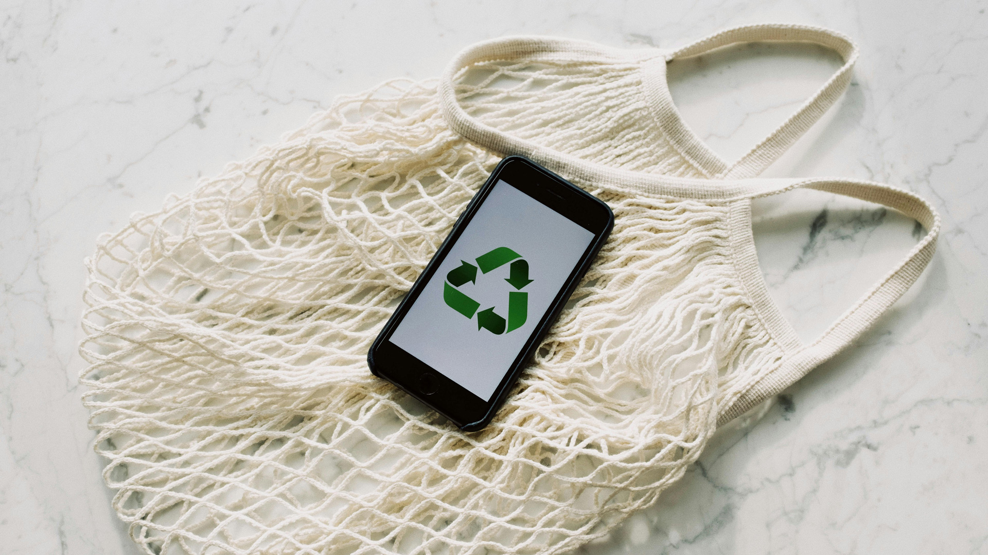 Image of a bag with a a phone on. The phone is showing the recycling symbol.