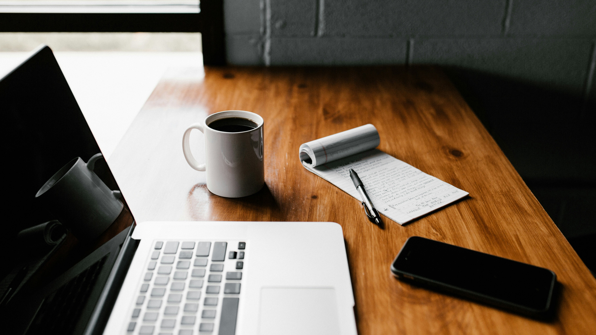 Image of laptop, coffee, phone and notepad on a table.