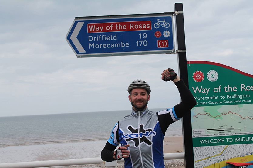 Photograph of man celebrating up Way of the Roses road sign